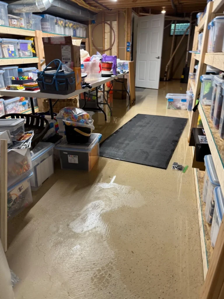 Wide view of flooded basement storage room with standing water on epoxy floor, tall wooden shelving units lined with plastic storage bins on both sides