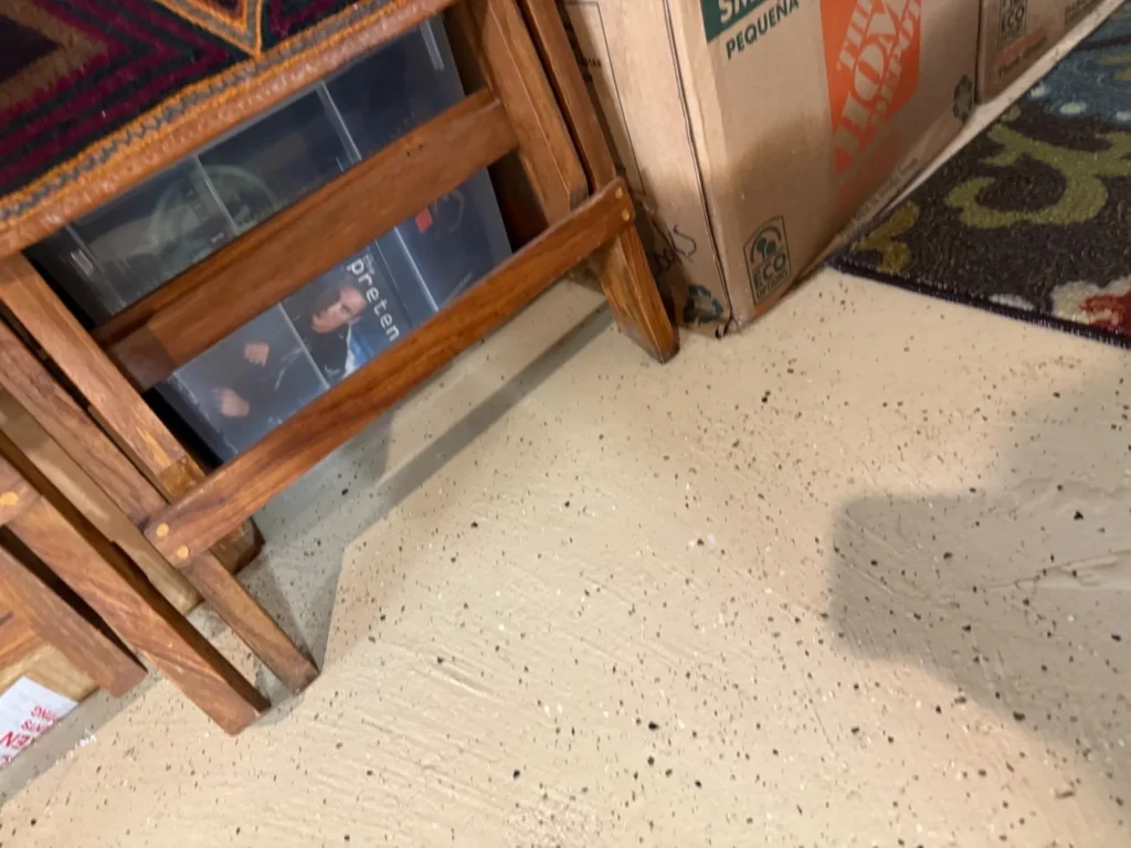 Close-up of wooden bookcase with DVDs and storage boxes sitting on wet epoxy basement floor with visible water damage