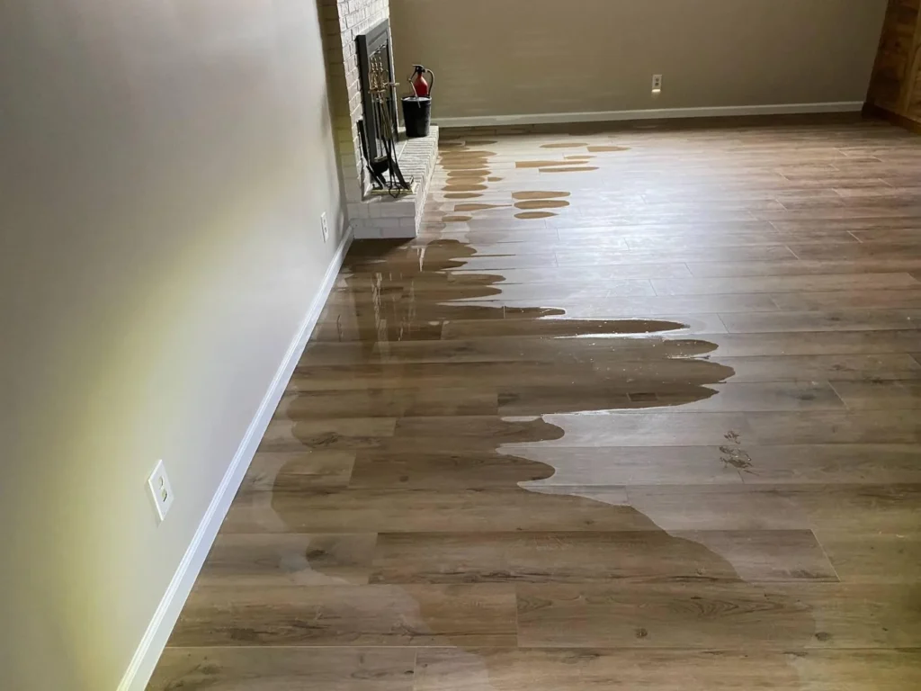 Living room with large puddles of standing water pooling on luxury vinyl plank flooring near brick fireplace after water damage event