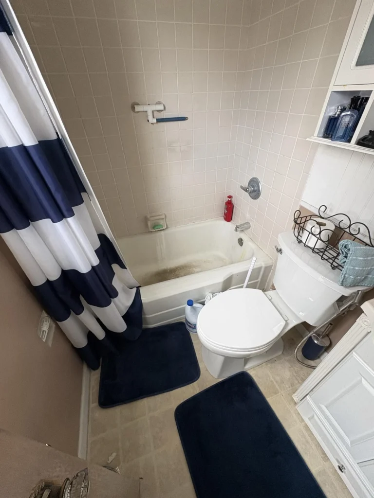 Overhead view of a bathroom showing a tub and shower with beige tile surround and dark stain in the tub basin, a toilet, and a white storage cabinet, identified as the water source for the ceiling leak in the unit below