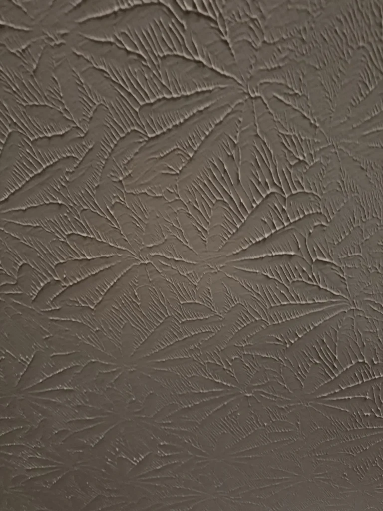 Close-up of textured ceiling showing extensive water damage with brown staining and dark discoloration spread across the entire surface, indicating significant moisture infiltration from above