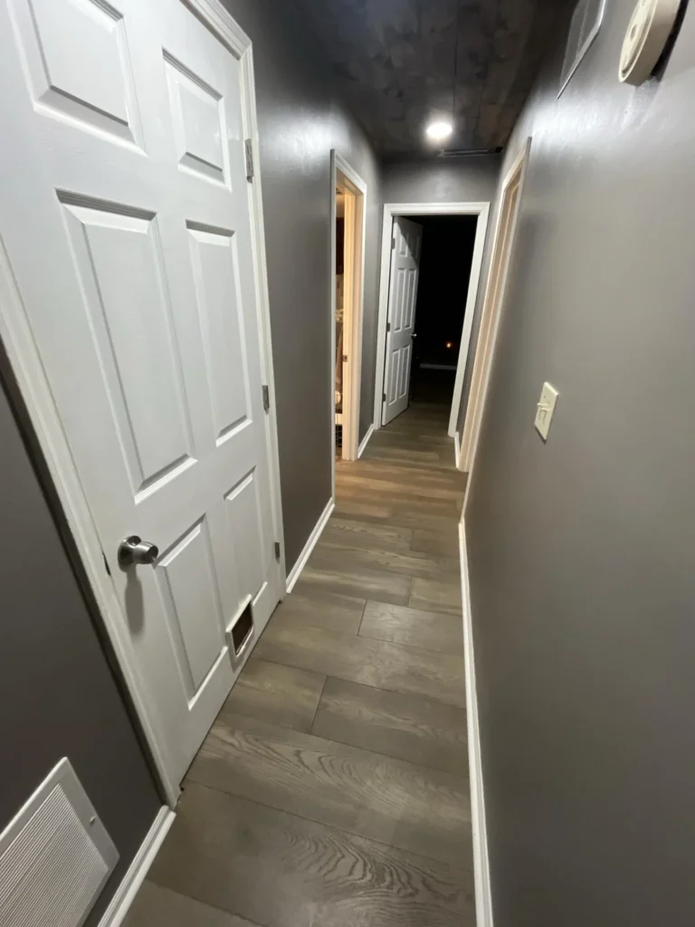 Residential hallway showing a white six-panel door, gray painted walls, wood-look luxury vinyl plank flooring, and white baseboards during a water damage restoration assessment