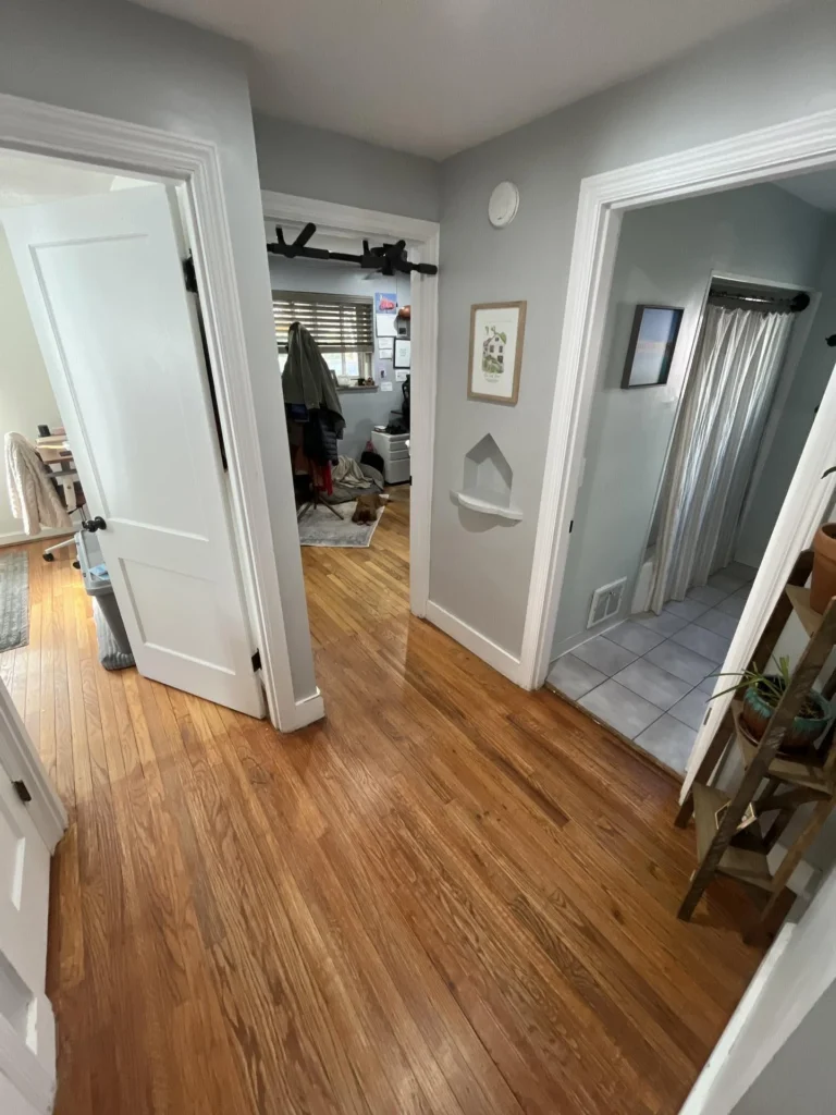Residential hallway with hardwood floors showing multiple white-painted doors leading to bedrooms and a bathroom, with a wall niche and neutral gray walls