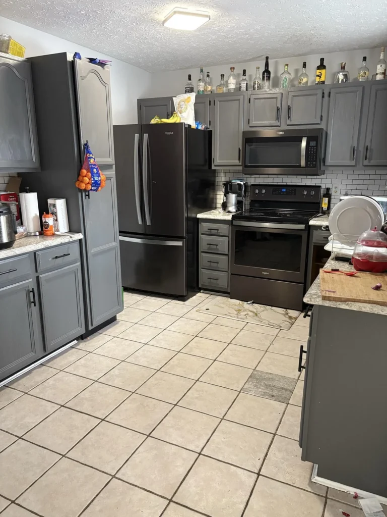 Kitchen with gray painted cabinets, black Whirlpool French door refrigerator and range, white subway tile backsplash, and water staining visible on the tile floor near the stove during an inspection